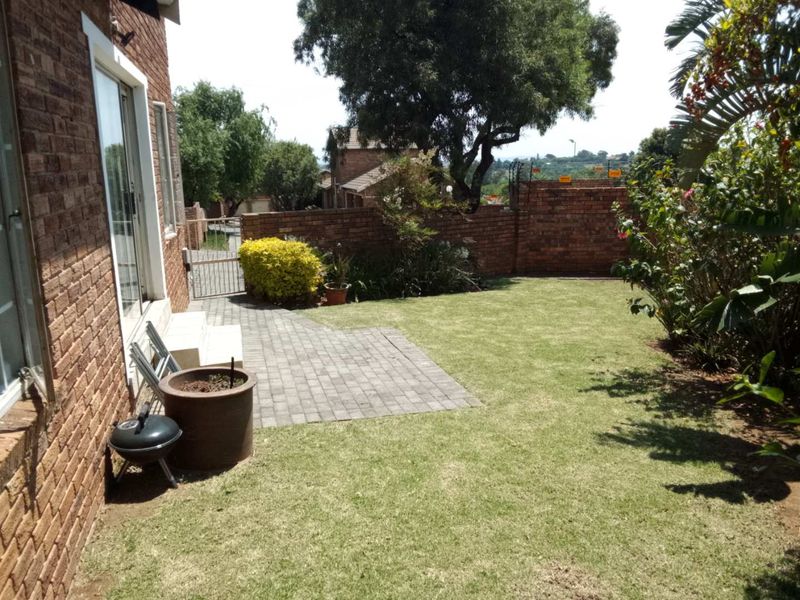 A private rear garden featuring a paved patio area, established lawn, and secure brick boundary walls with electric fencing.