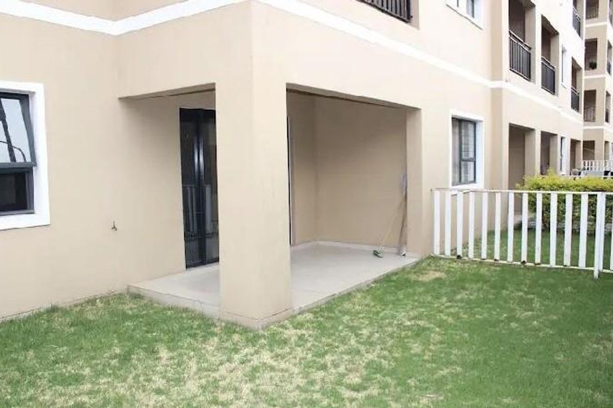 Ground floor apartment featuring a covered patio area with direct access to a private lawn and enclosed by a white picket fence.