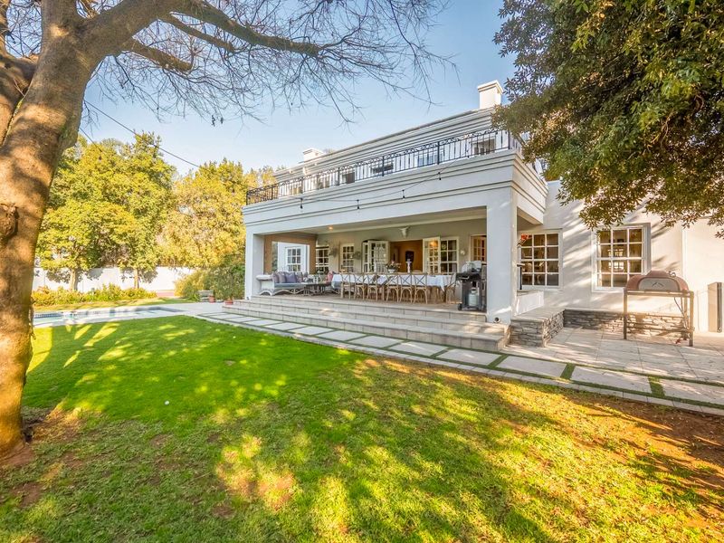 Rear view of the property featuring a spacious covered patio, upper balcony with wrought iron railing, swimming pool, and landscaped garden area.