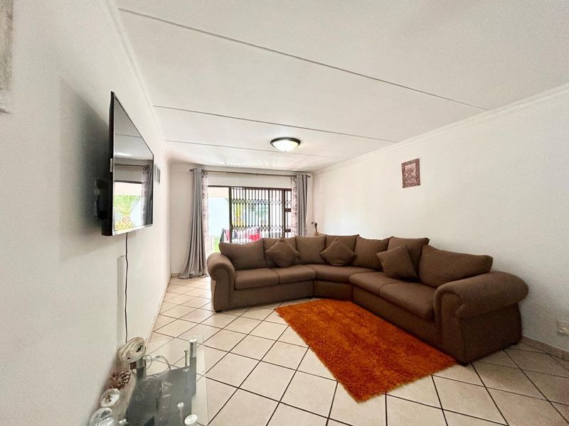 A living room featuring tiled flooring, a ceiling light fixture, and a sliding door with a security gate leading to the exterior.