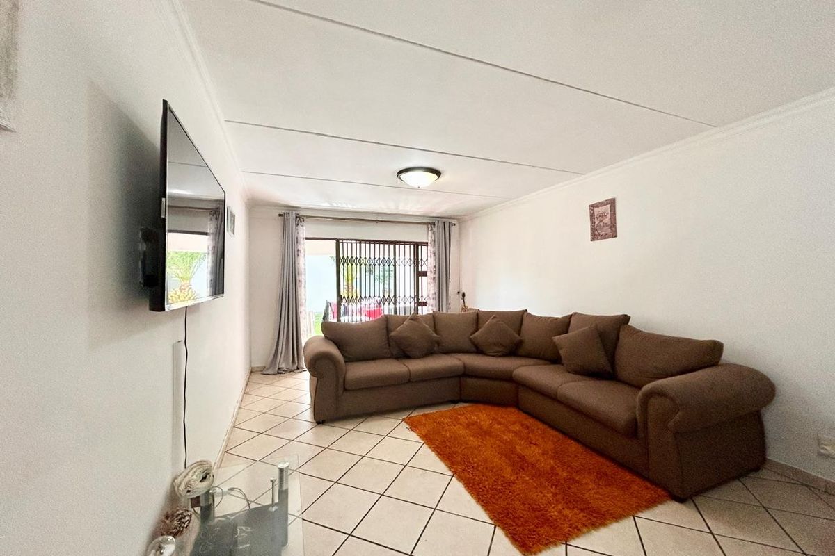 A living room featuring tiled flooring, a ceiling light fixture, and a sliding door with a security gate leading to the exterior.