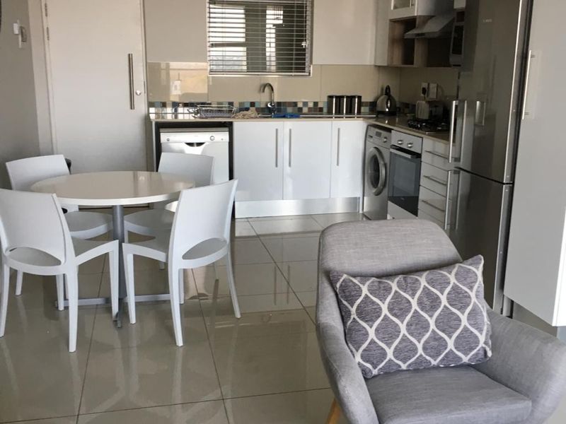 An open-plan kitchen and dining area featuring modern white cabinetry, tiled flooring, and integrated appliances, creating a functional and cohesive living space.