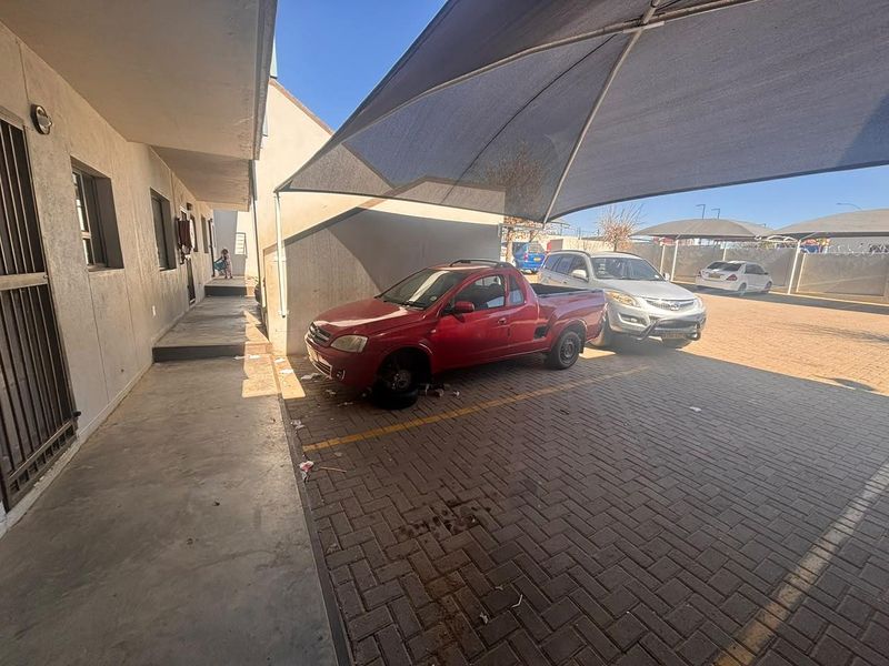 Outdoor parking area featuring a shade cloth carport structure and paved driveway surface adjacent to the apartment building entrance.