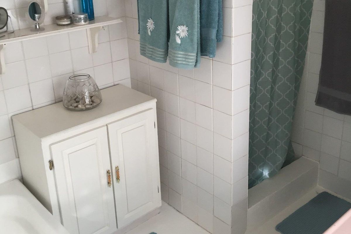 A functional bathroom featuring a built-in vanity cabinet, tiled wall finishes, and a shower area with a privacy partition.