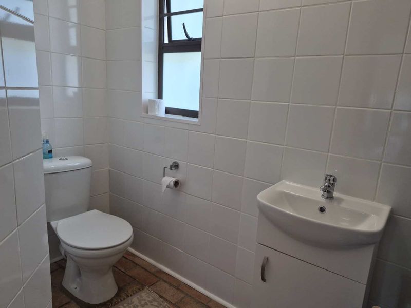 A compact bathroom featuring white wall tiles, a modern vanity basin with mixer tap, and a standard toilet.