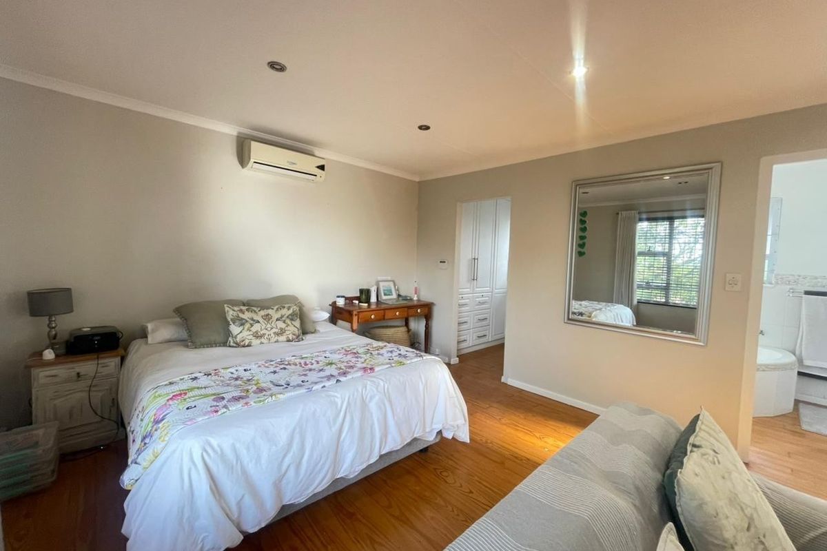 A well-maintained bedroom featuring hardwood flooring, recessed lighting, an integrated air conditioning unit, and convenient access to an en-suite bathroom.