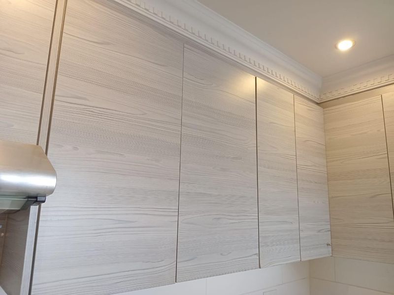 A close-up view of modern light wood-grain kitchen cabinetry featuring integrated extractor fan and decorative crown molding.