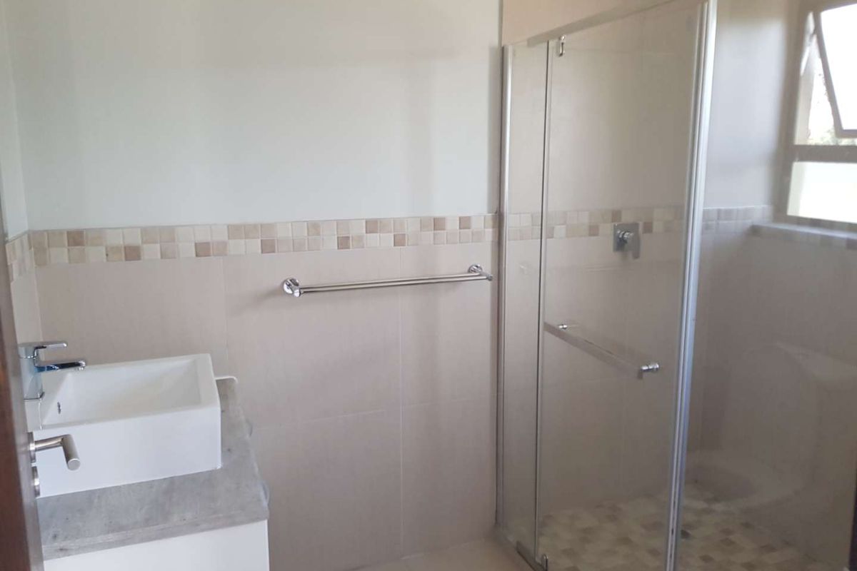 A modern bathroom featuring a glass-enclosed shower, a vessel sink vanity, and neutral wall tiling with a decorative mosaic border.