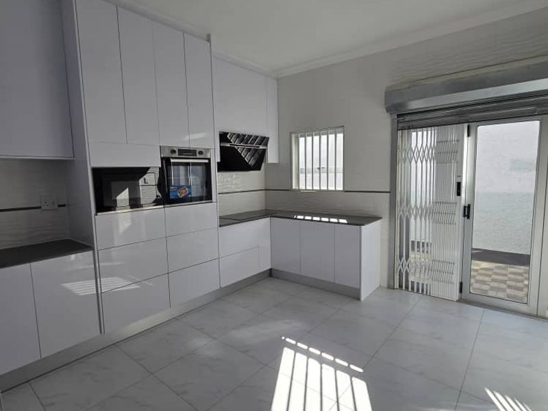 Modern kitchen featuring high-gloss white cabinetry, built-in appliances, stone countertops, and direct access to an outdoor area through a secure sliding door.