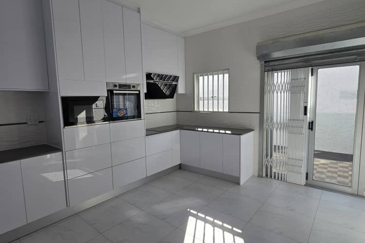 Modern kitchen featuring high-gloss white cabinetry, built-in appliances, stone countertops, and direct access to an outdoor area through a secure sliding door.