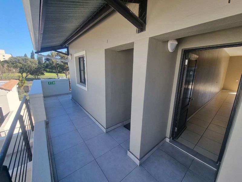 A clean, covered balcony area featuring tiled flooring, a metal balustrade, and direct access to the interior of the apartment.