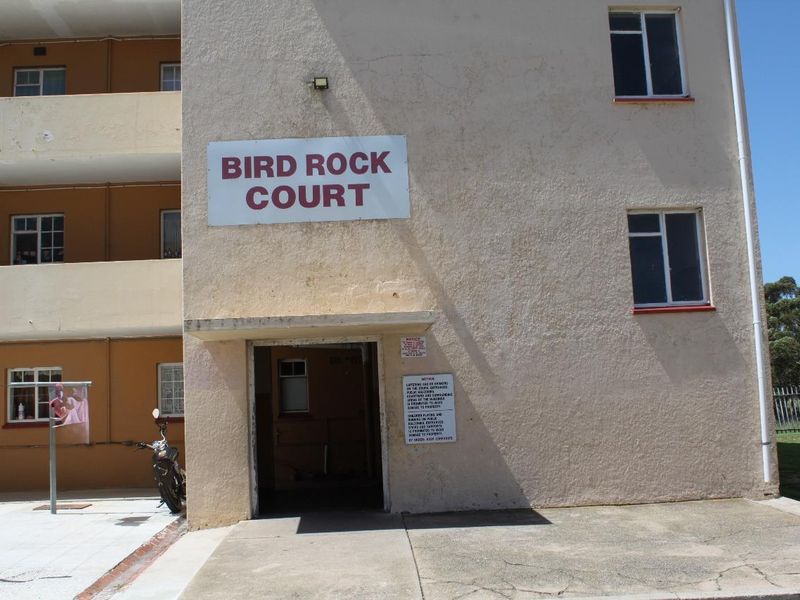 Exterior view of the Bird Rock Court apartment building entrance, featuring a stucco facade and concrete walkway.