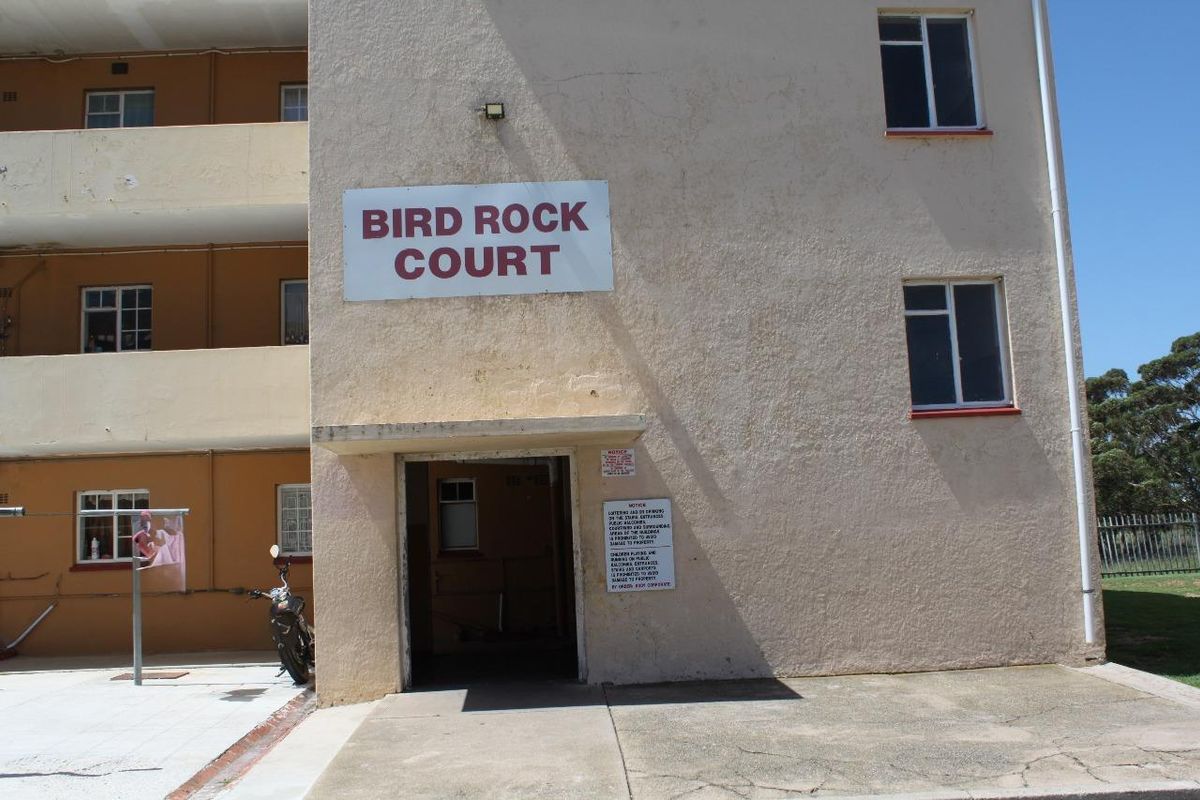 Exterior view of the Bird Rock Court apartment building entrance, featuring a stucco facade and concrete walkway.