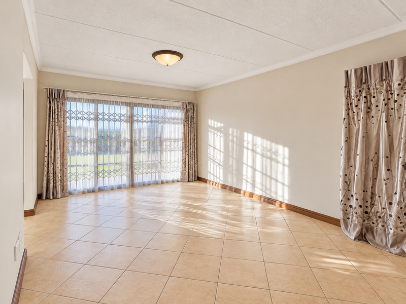 A bright and spacious living room featuring neutral ceramic tile flooring, large sliding glass doors with security gates, and a clean, minimalist aesthetic.