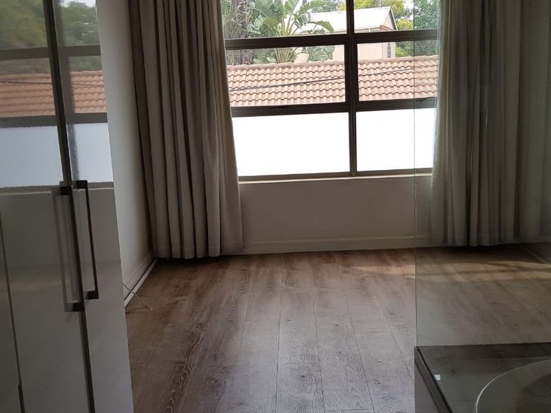 A bright and spacious bedroom featuring modern laminate flooring, built-in cupboards, and a large window allowing for ample natural light.