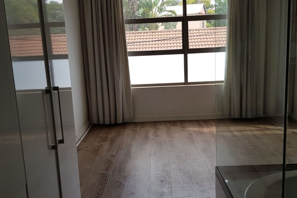 A bright and spacious bedroom featuring modern laminate flooring, built-in cupboards, and a large window allowing for ample natural light.