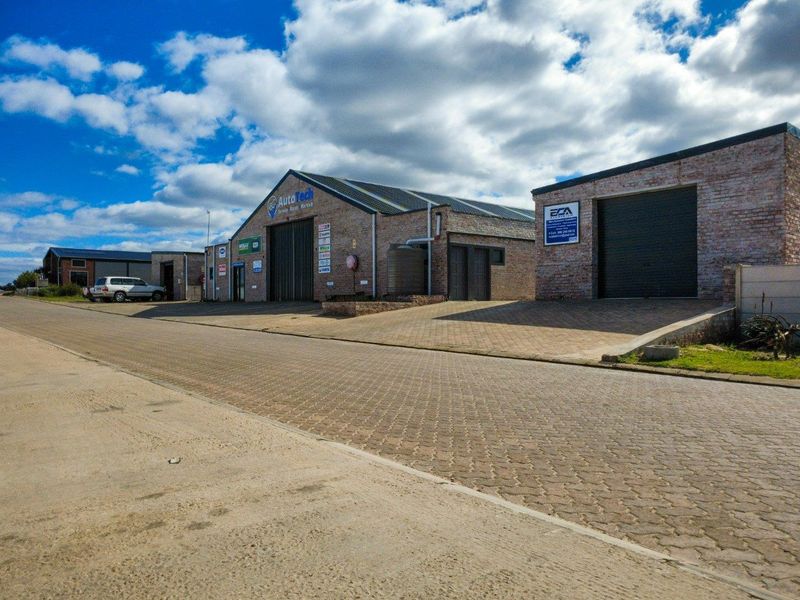 Front exterior view of a commercial industrial property featuring brick construction, roller shutter doors, and a paved driveway area.