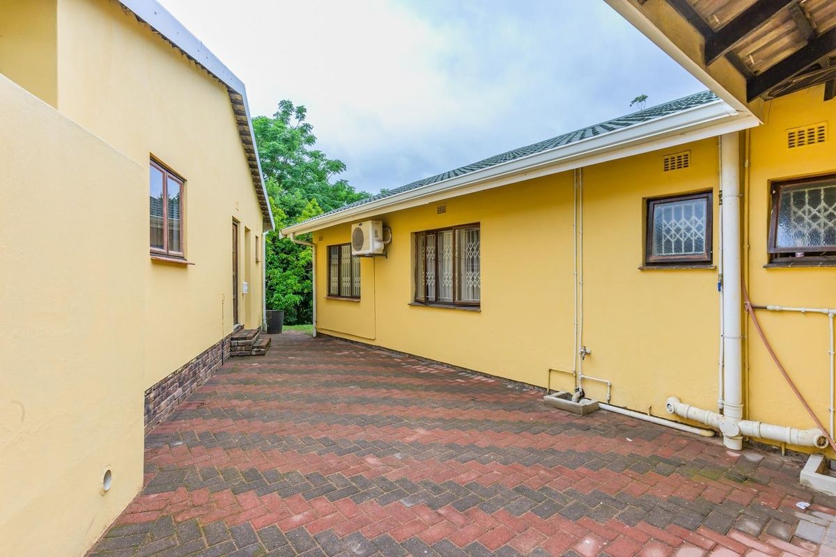 A rear exterior view of the property featuring brick paving, plastered walls, and security bars on the windows.