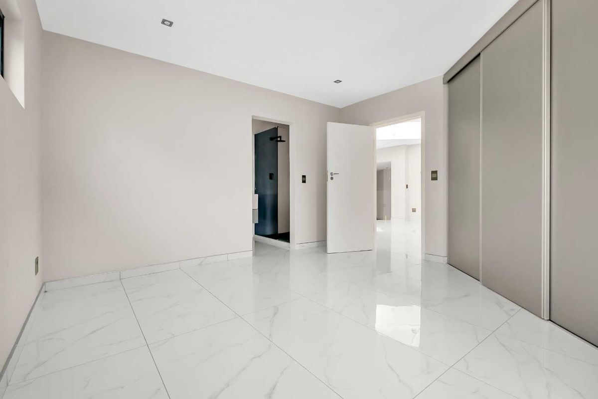 A bright, modern bedroom featuring polished marble-look floor tiles, built-in sliding door wardrobes, and an en-suite bathroom entrance.