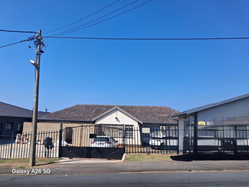 Front elevation of a single-story house featuring a tiled roof, secure metal perimeter fencing, and a gated driveway entrance.