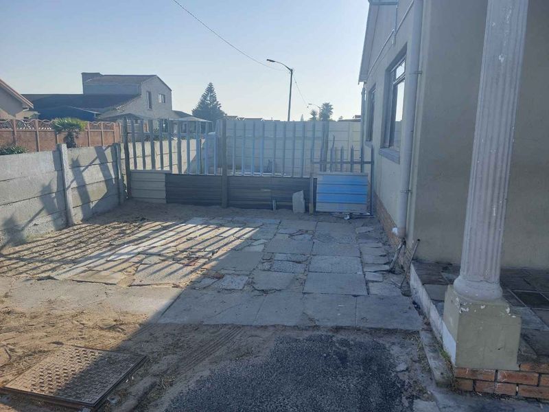 Rear exterior area featuring paved ground, boundary walling, and metal gate access, requiring maintenance and landscaping improvements.