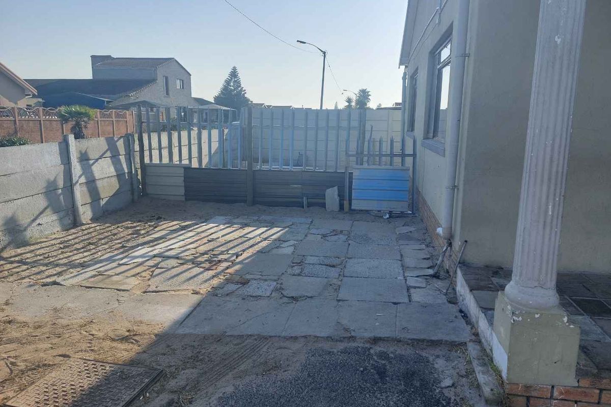 Rear exterior area featuring paved ground, boundary walling, and metal gate access, requiring maintenance and landscaping improvements.