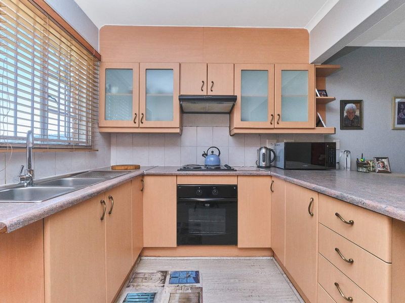 A functional U-shaped kitchen featuring light wood-tone cabinetry, laminate countertops, a built-in oven with gas hob, and a double stainless steel sink.