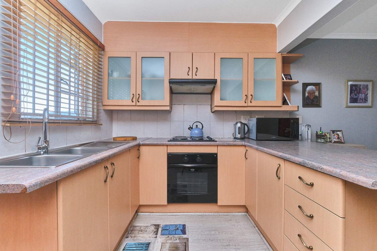 A functional U-shaped kitchen featuring light wood-tone cabinetry, laminate countertops, a built-in oven with gas hob, and a double stainless steel sink.