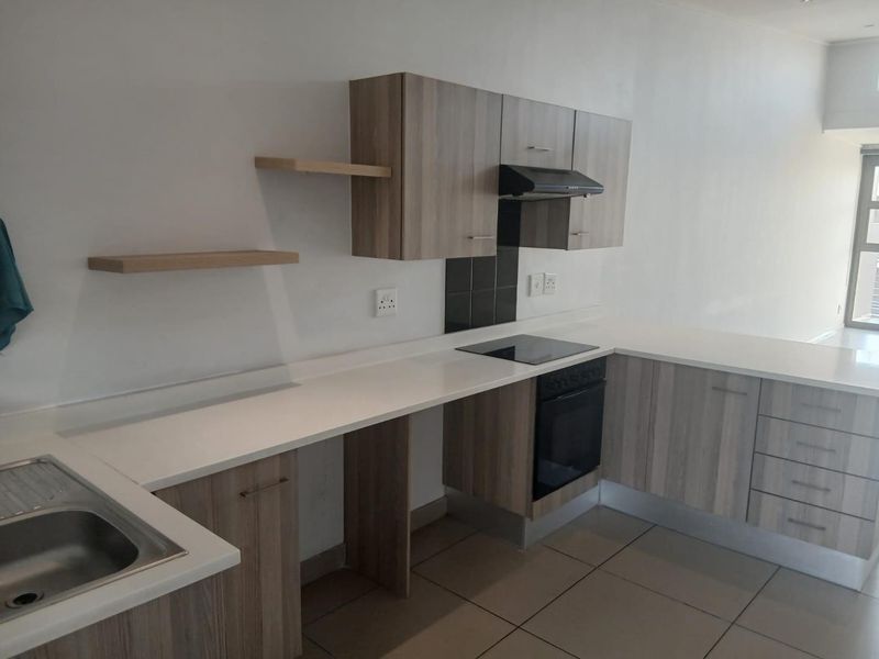 Modern kitchen featuring light wood-grain cabinetry, white countertops, integrated oven and hob, and neutral floor tiles in an open-plan layout.
