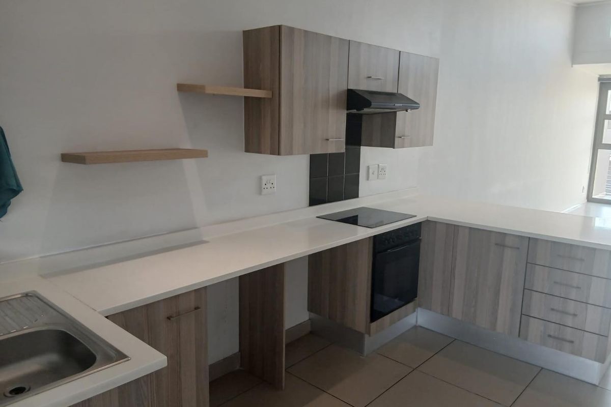 Modern kitchen featuring light wood-grain cabinetry, white countertops, integrated oven and hob, and neutral floor tiles in an open-plan layout.
