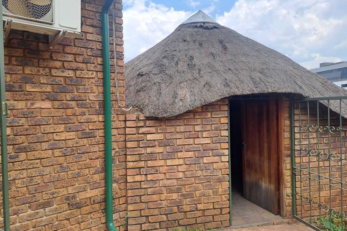 Exterior view of a traditional thatched-roof structure with exposed brick walls, featuring an entrance door and an external air conditioning unit.