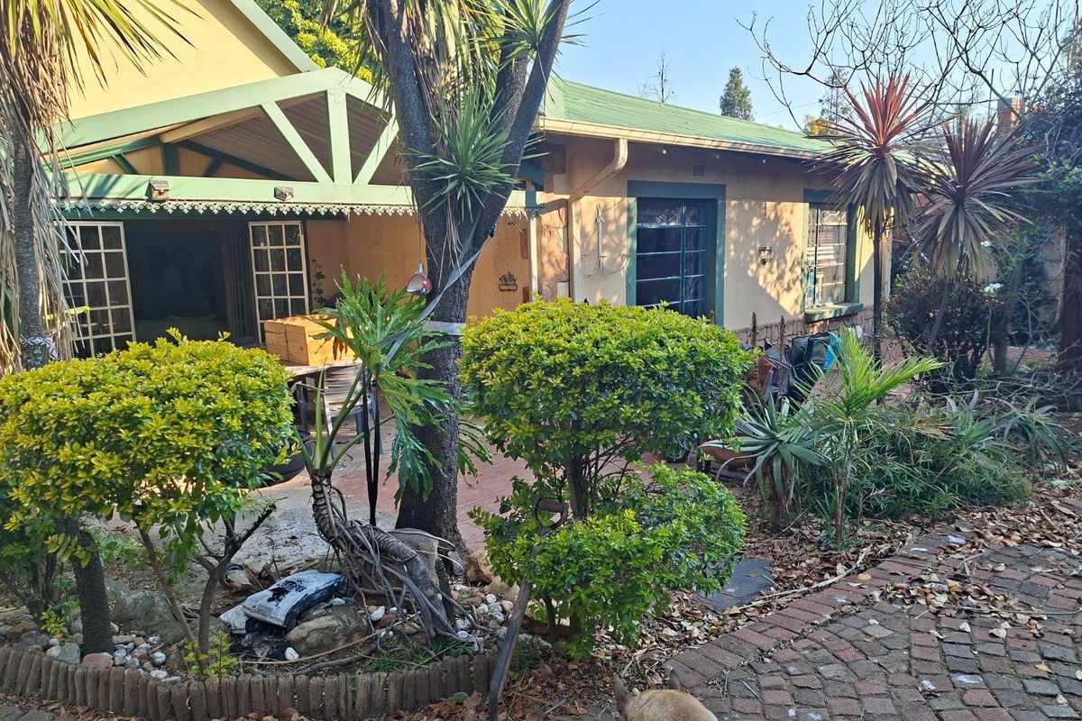 Rear view of the property featuring a covered patio area, brick paving, and established garden landscaping with mature trees and shrubs.