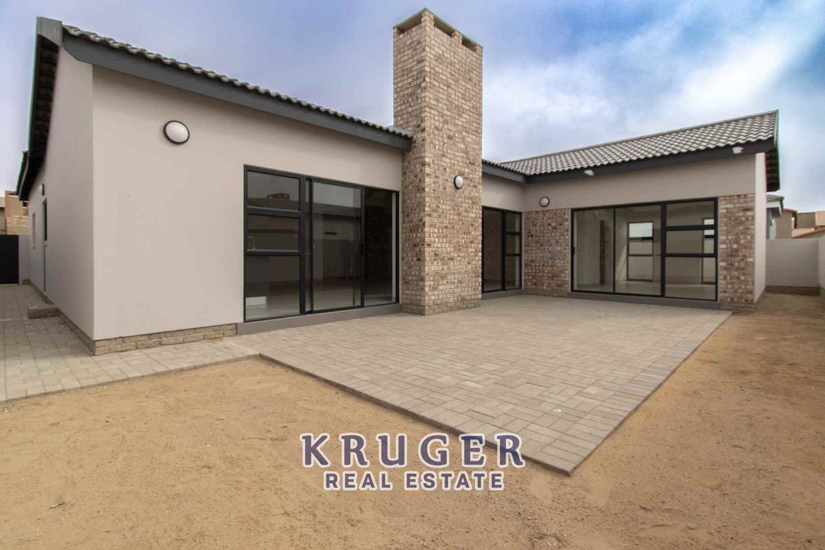 Rear view of the property featuring a paved patio area, brick chimney stack, and large sliding glass doors leading into the home.