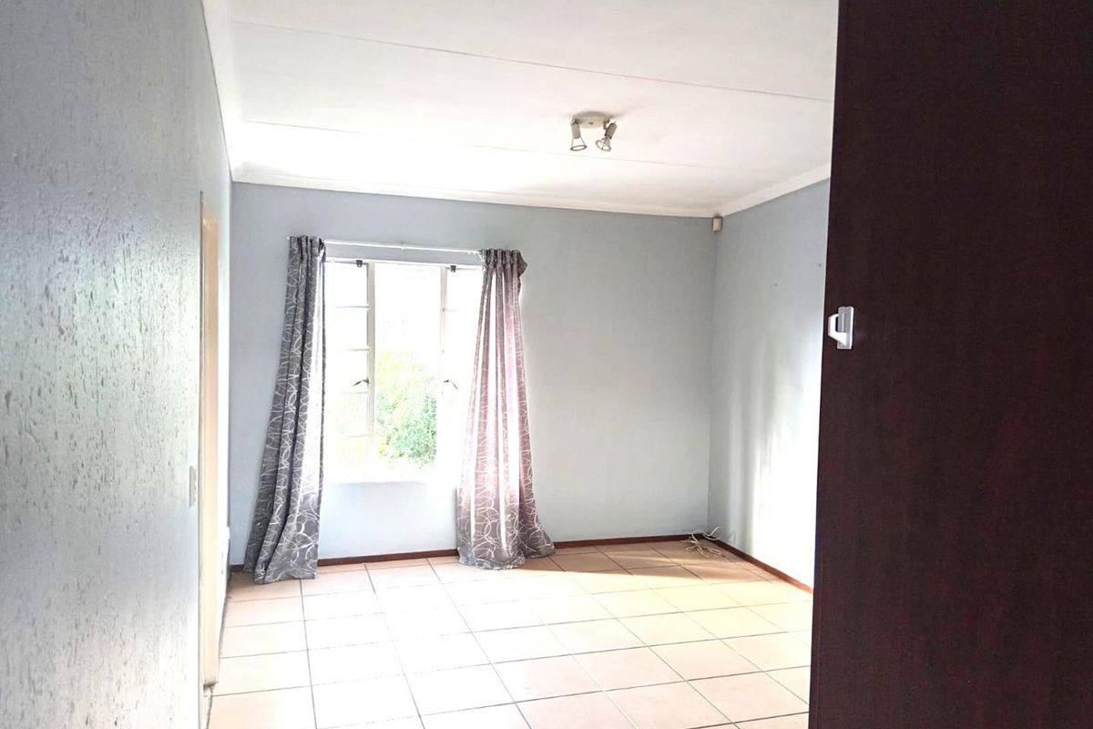 A vacant bedroom featuring neutral tiled flooring, light blue walls, and a window providing natural light.