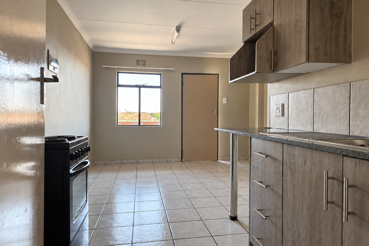 A functional kitchen featuring wood-look cabinetry, tiled flooring, a tiled backsplash, and a freestanding stove, offering a clean and practical layout.