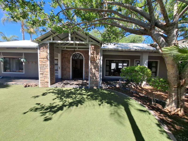 A well-maintained rear exterior view featuring a covered patio with stone cladding, a corrugated metal roof, and a neatly landscaped artificial lawn area.