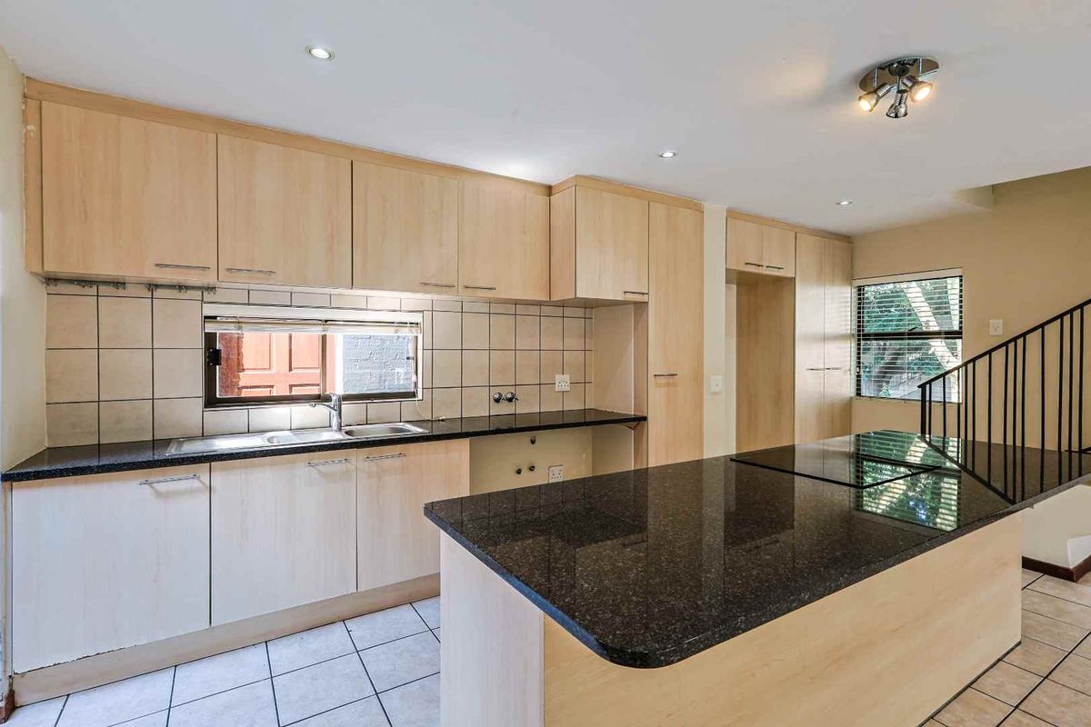 A functional kitchen featuring light wood cabinetry, dark granite countertops, a breakfast bar, and tiled flooring, with an open-plan layout.