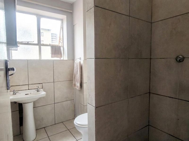 A functional bathroom featuring a pedestal basin, toilet, and a tiled shower enclosure with neutral wall and floor tiling.