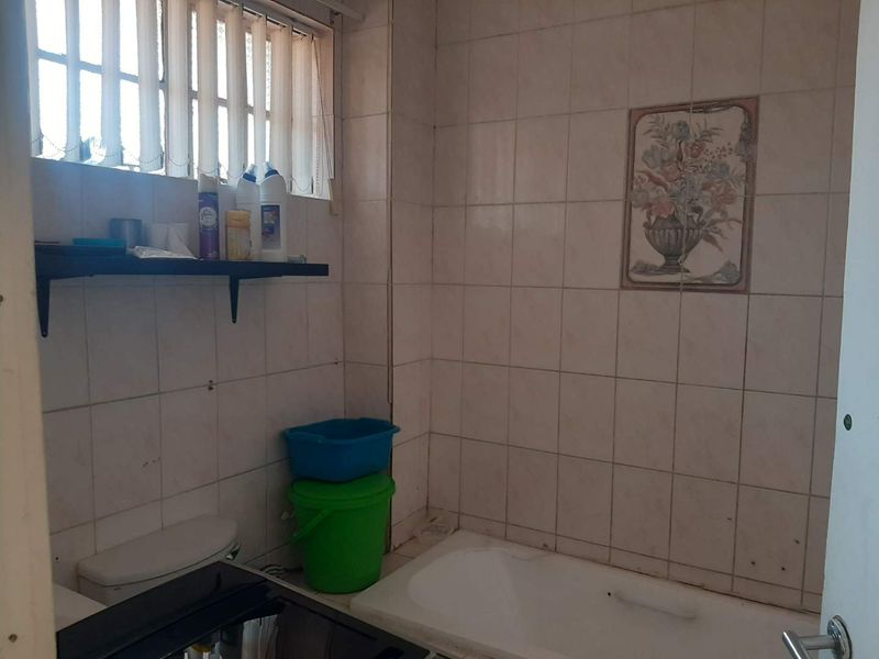 A dated bathroom featuring a bathtub, toilet, and full-height wall tiling, requiring cosmetic updates to modernize the space.