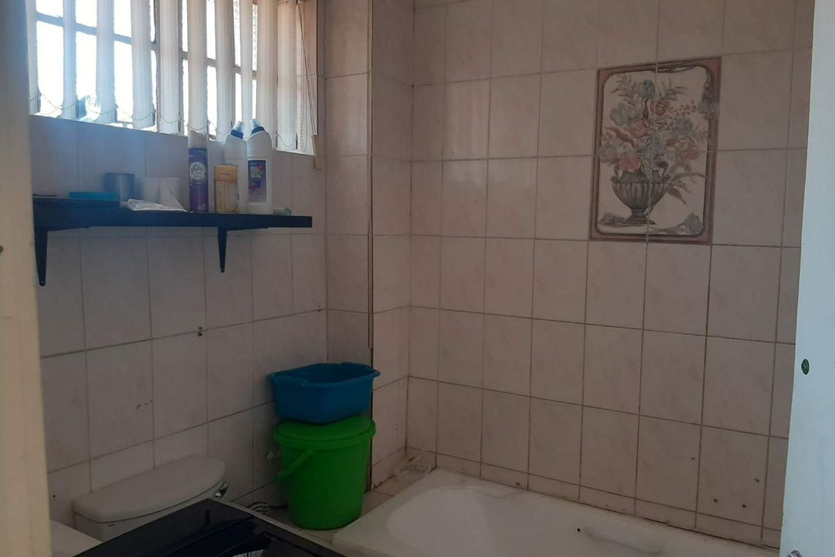 A dated bathroom featuring a bathtub, toilet, and full-height wall tiling, requiring cosmetic updates to modernize the space.