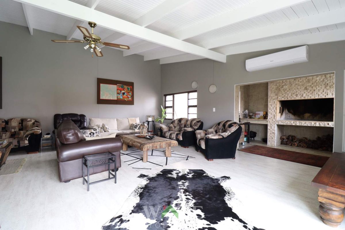 Spacious living room featuring a vaulted beamed ceiling, built-in stone fireplace, and wall-mounted air conditioning unit.
