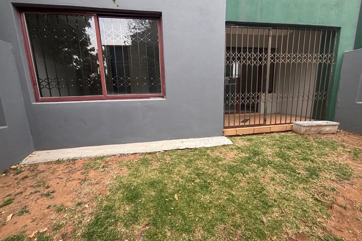 Rear exterior view of the apartment featuring a small patio area with security gates and a patch of lawn.