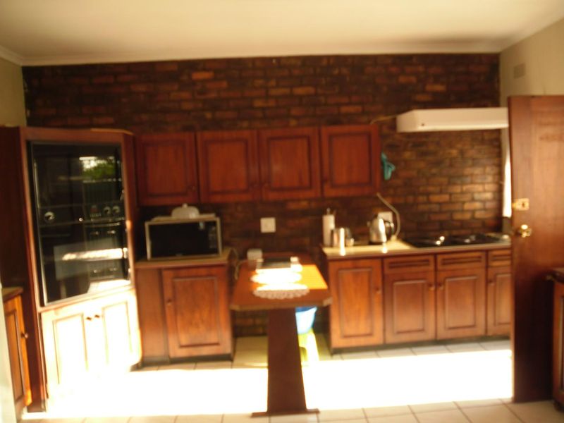 A dated kitchen featuring dark wood cabinetry, an exposed brick feature wall, built-in oven, and cooktop with tiled flooring.
