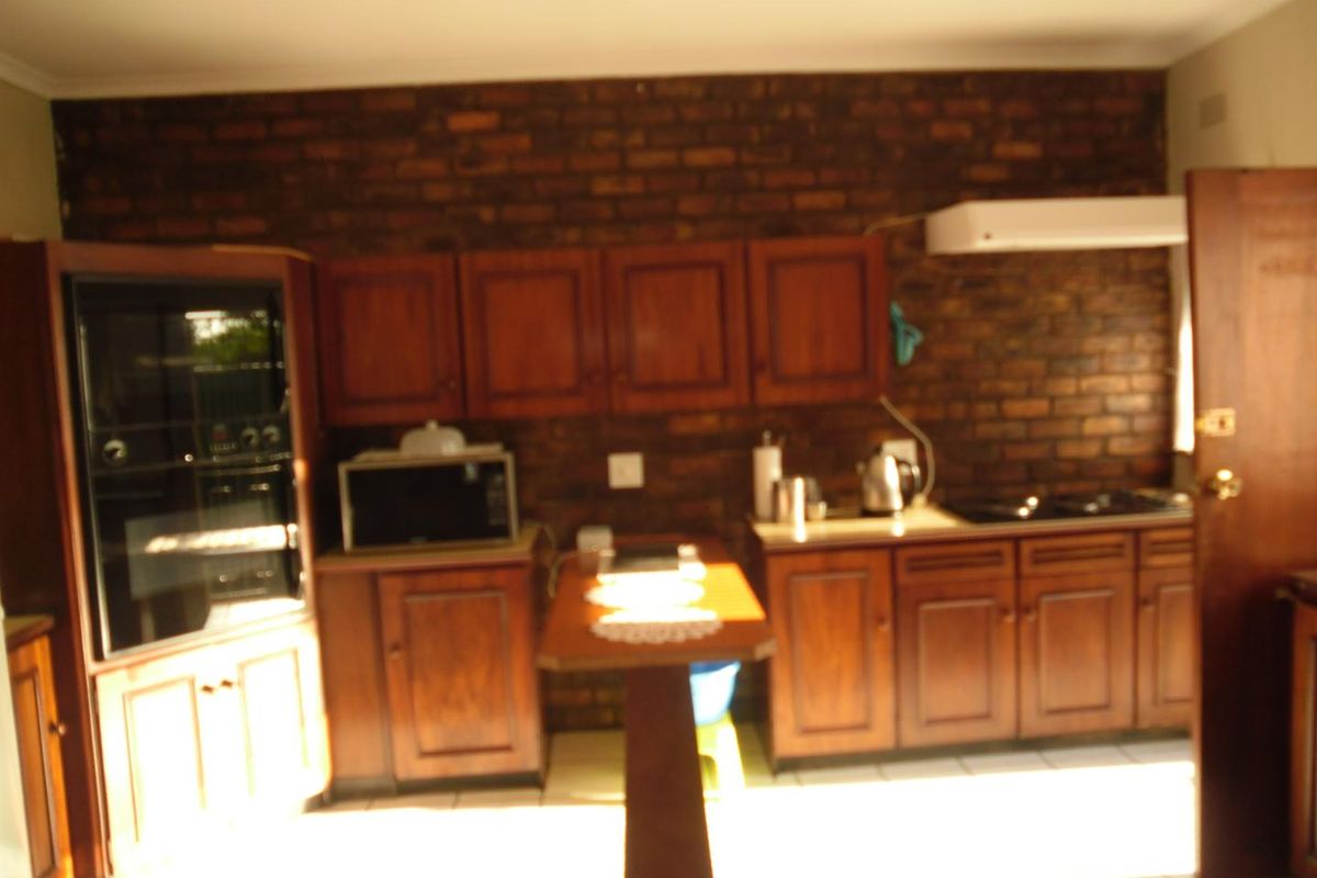 A dated kitchen featuring dark wood cabinetry, an exposed brick feature wall, built-in oven, and cooktop with tiled flooring.