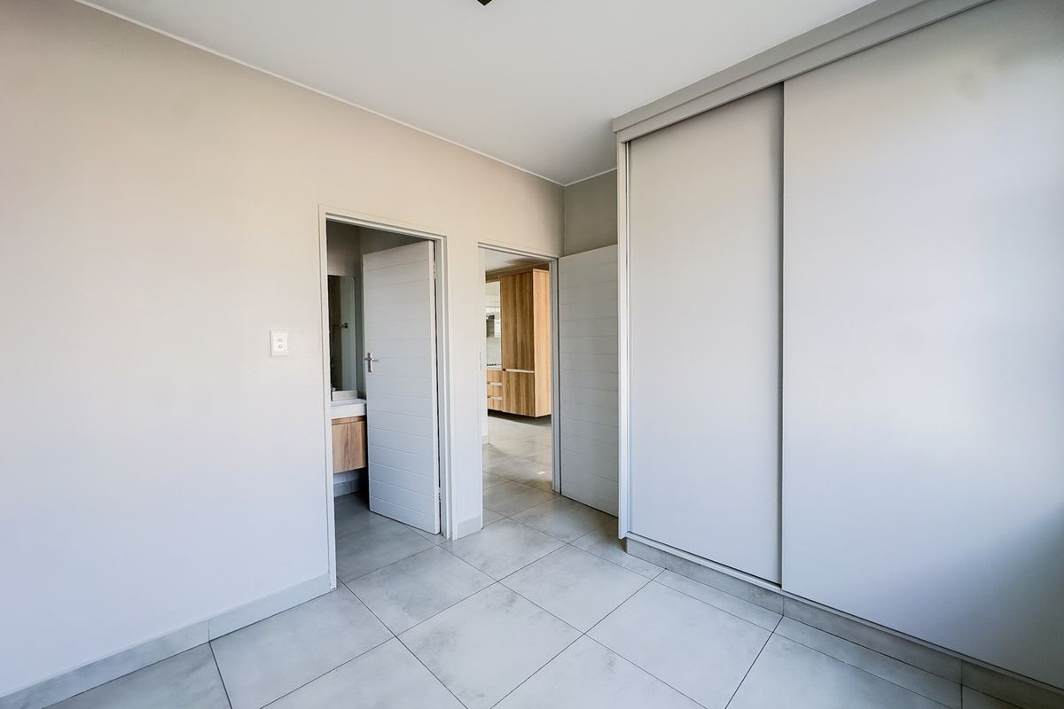 A clean, modern bedroom featuring large format floor tiles, neutral walls, and a spacious built-in sliding door wardrobe.
