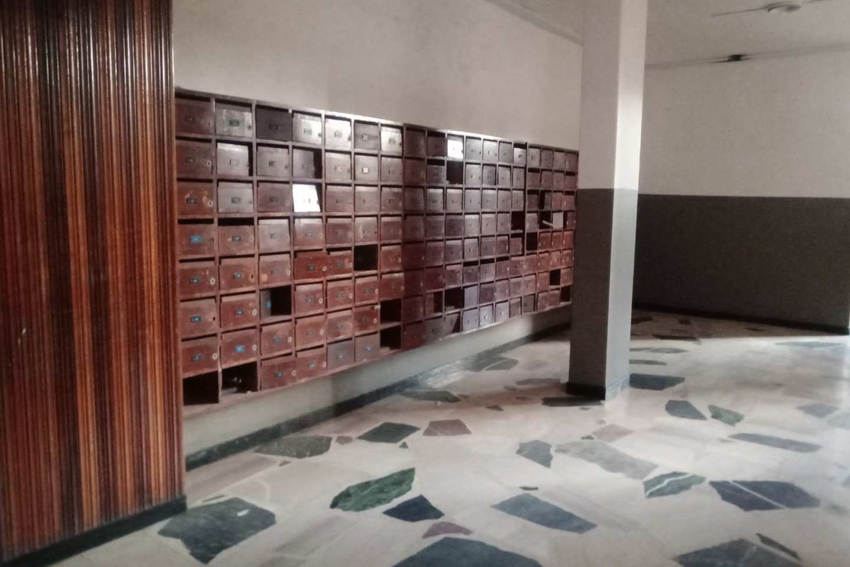 A communal apartment building lobby featuring a large wall of built-in mailboxes, terrazzo flooring, and wood-paneled accents.