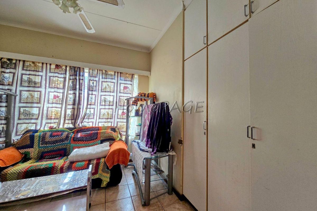 A bedroom featuring built-in floor-to-ceiling cupboards, tiled flooring, and a ceiling fan, offering functional storage space.