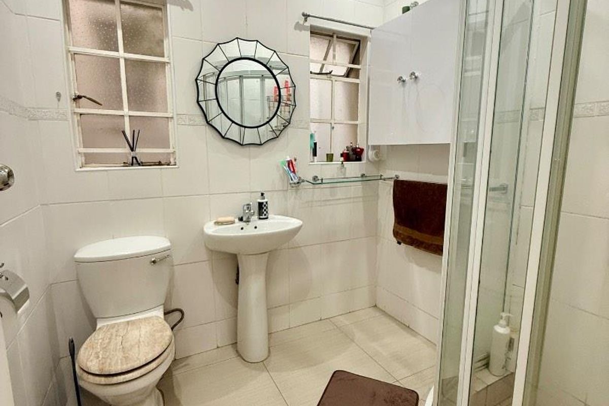 A functional bathroom featuring a pedestal basin, a corner shower enclosure with glass doors, and a standard toilet.