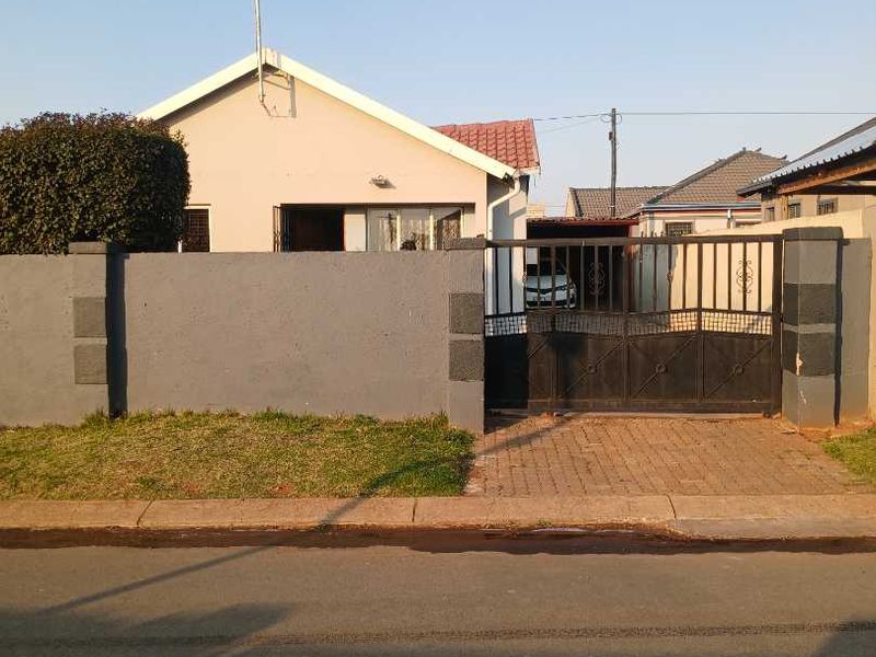 Front view of a residential house featuring a paved driveway, secure metal gate, and perimeter walling.