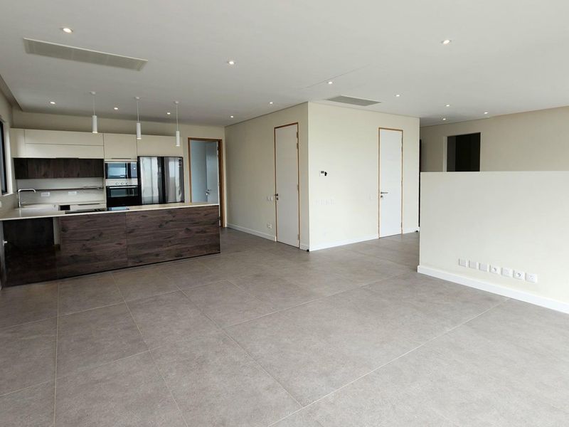 Spacious open-plan living area featuring a modern kitchen with integrated appliances, sleek cabinetry, stone countertops, and neutral tiled flooring throughout.